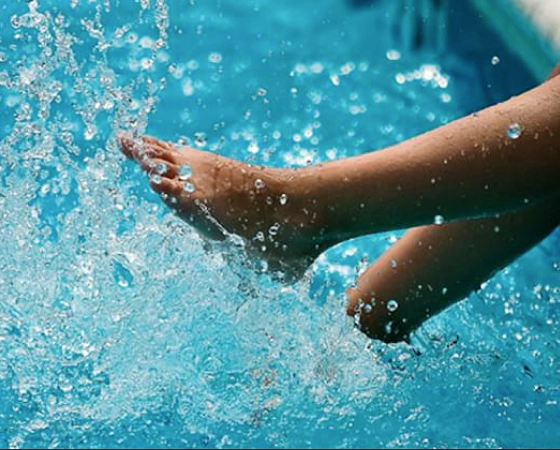 little girl dipping feet into pool and splashing